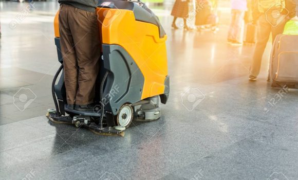 Man driving professional floor cleaning machine at airport or railway station.  Floor care and cleaning service agency.