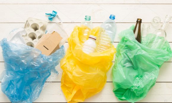 Recycling and ecology. Sorting (segregating) household waste (paper, glass, plastic) into bags captured from above (flat lay). White wooden background.